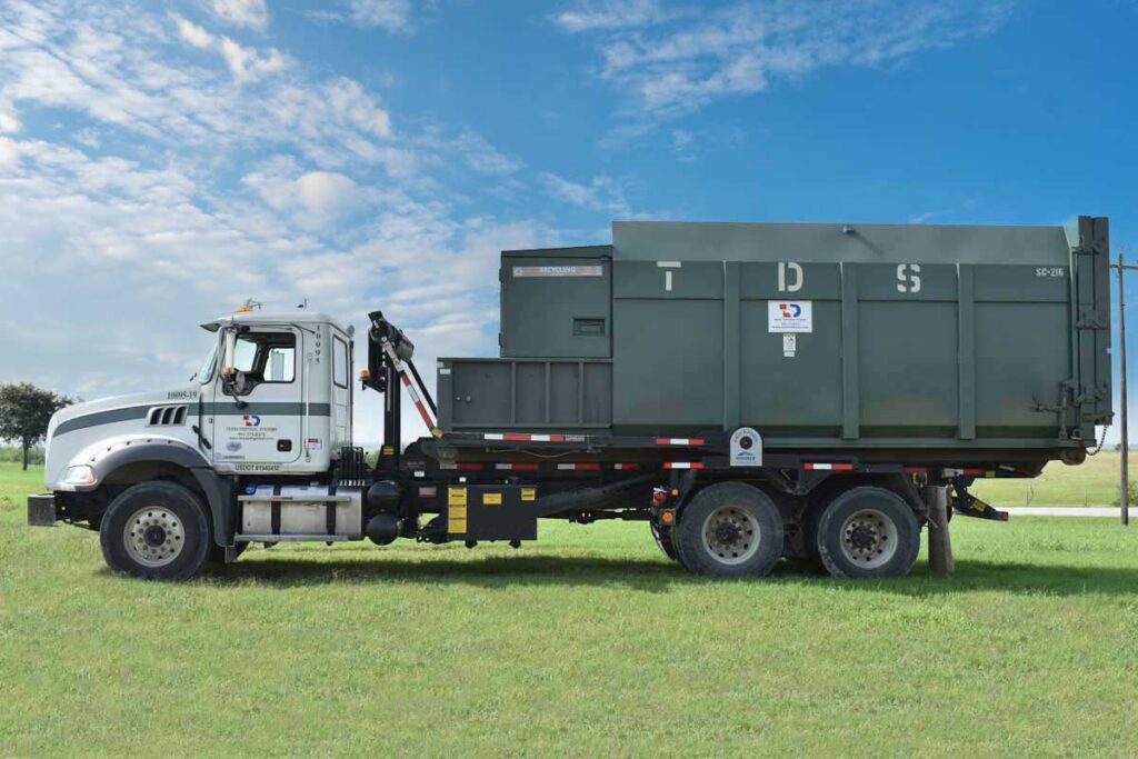 Green TDS compactor roll off dumpster parked in a field of grass
