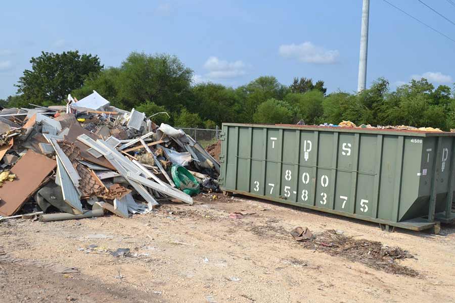 TDS green roll off dumpster next to pile of disaster debris for disaster clean up