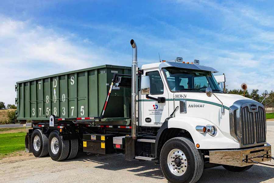 Green Roll off dumpster on TDS truck parked under blue sky