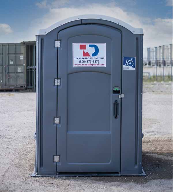 A single gray ADA unit in a gravel yard