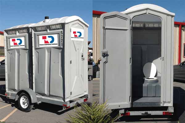 Two gray portable restroom units sitting side by side next to each other on a small trailer with tires