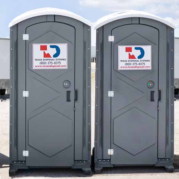 Two gray standard portable restroom units sitting side by side next to each other