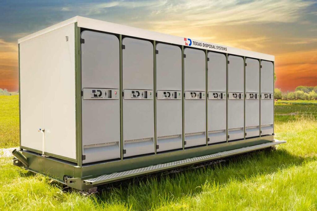 Row of gray 8x8 multi-stall restroom units in a field during sunset