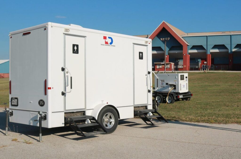 A portable restroom trailer with men and women’s door labels sits next to a portable generator at the Travis County Expo Center