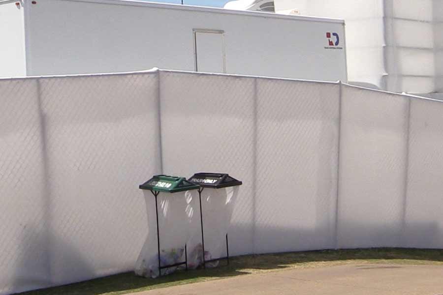 Temporary fence with high white privacy screens behind two event waste containers