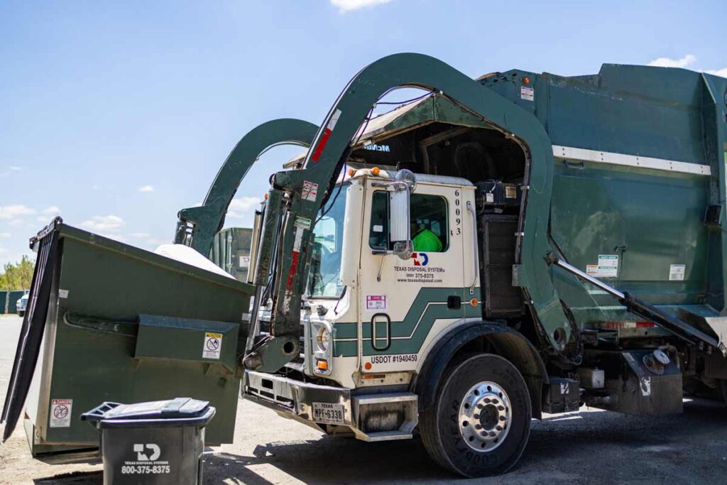 Green commercial TDS front load truck being picked up my TDS truck with TDS cart