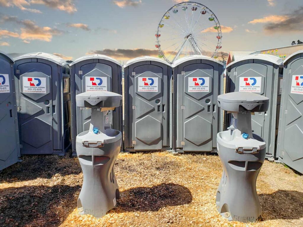 A row of TDS portable restroom units and handwashing stations with a ferris wheel in the background