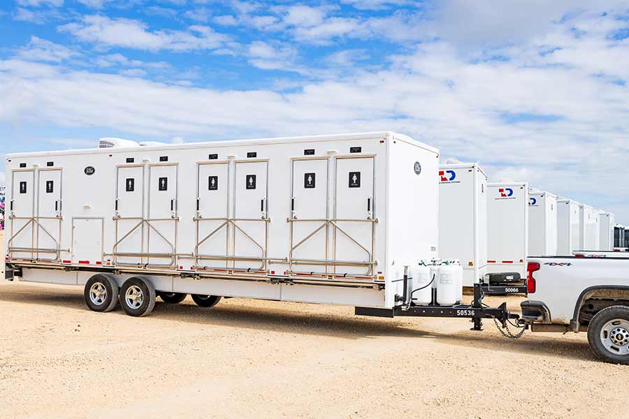 White TDS restroom trailers attached to a truck among multiple trailers parked in a lot