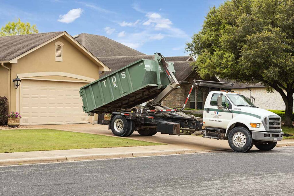 Green TDS mini roll off dumpster being delivered from a TDS truck in front of house onto driveway