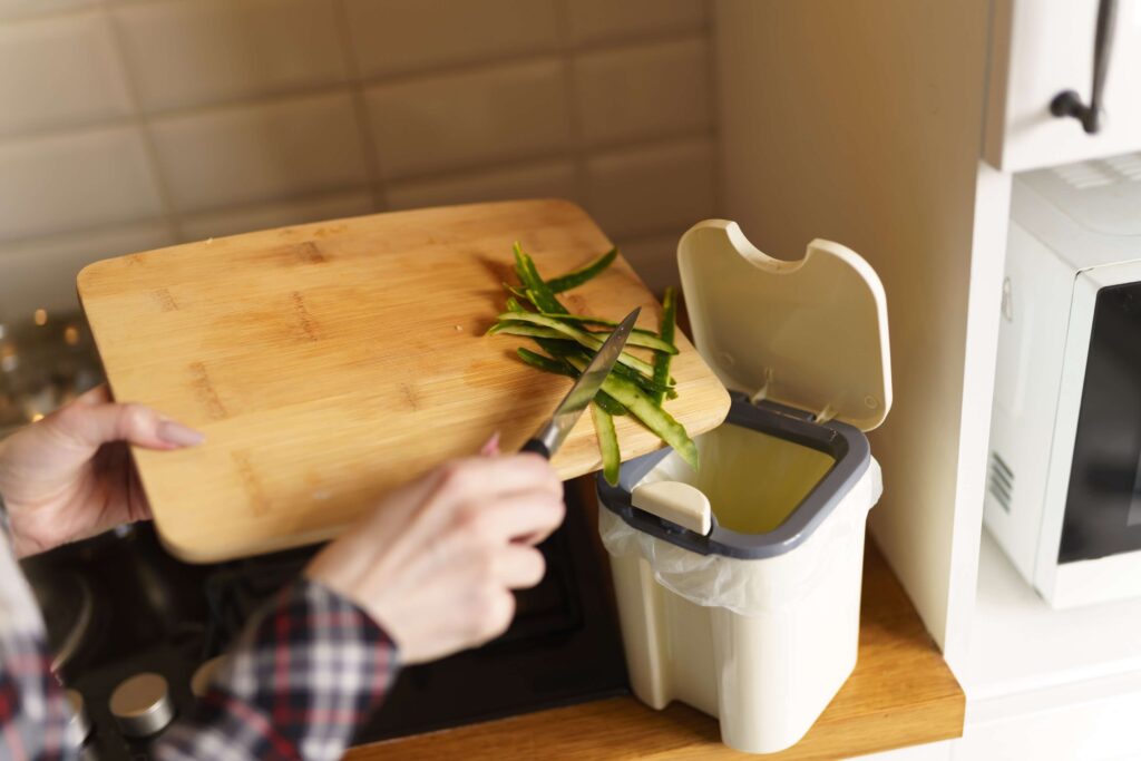 person scraping food scraps into compost bin in their apartment off cutting board