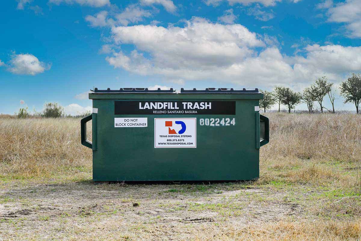 TDS green 2 yard front dumpster for landfill trash sitting in field