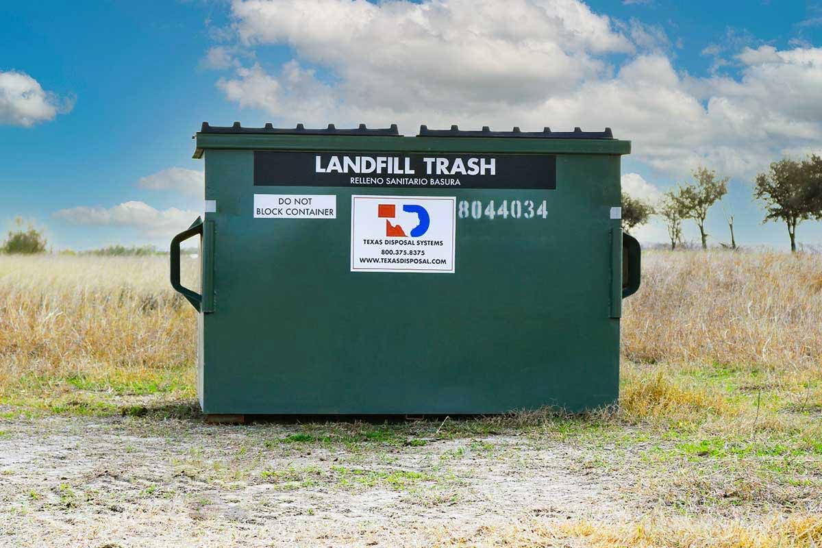 TDS green 4 yard front dumpster for landfill trash sitting in field