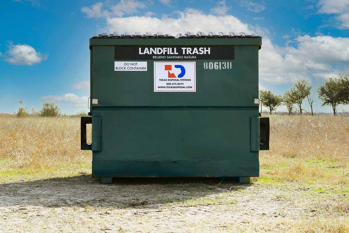 TDS green 6 yard front dumpster for landfill trash sitting in field