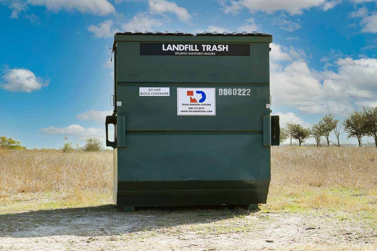 TDS green 8 yard front dumpster for landfill trash sitting in field